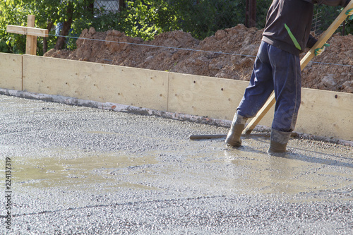 worker in rubber boots stands in uncluttered cement and leveling the surface of the base plate (fresh concrete slab) with a special wooden working tool © sommersby
