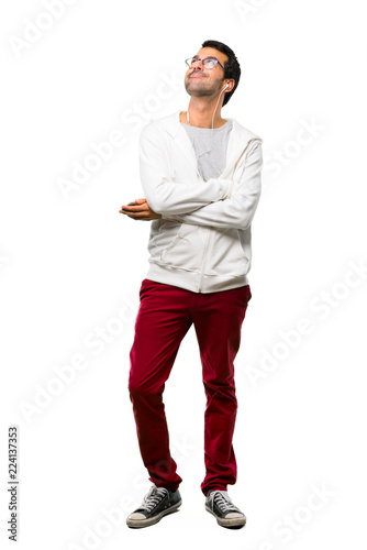 A full-length shot of a Man with glasses and listening music stand and looking up while smiling on white background © luismolinero
