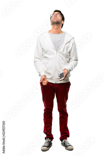 A full-length shot of a Man with glasses and listening music stand and looking up with serious face on white background