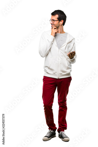 A full-length shot of a Man with glasses and listening music standing and looking to the side with the hand on the chin on white background