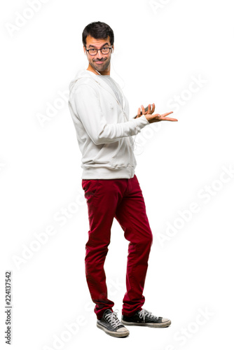 Full body of Man with glasses and listening music presenting a product or an idea while looking smiling towards on white background