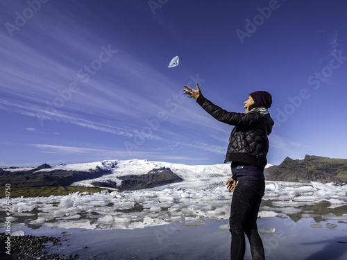 Woman throwing a piece of glacier ice into the air in glacier lagoon in Iceland