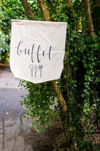 Buffet raw fabric hanging sign written in vintage stylish calligraphy font hanging from a tree in a garden © Putthipong