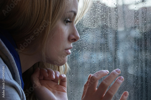 Фотография sad young woman looking through window on rainy day