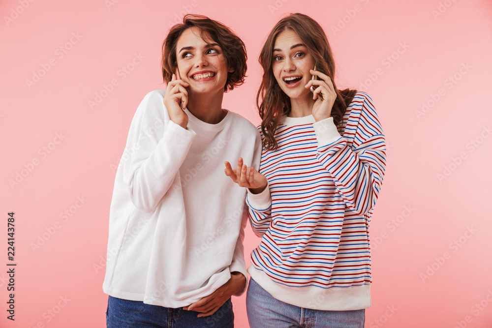 Fototapeta premium Women friends isolated over pink wall background talking by mobile phones.
