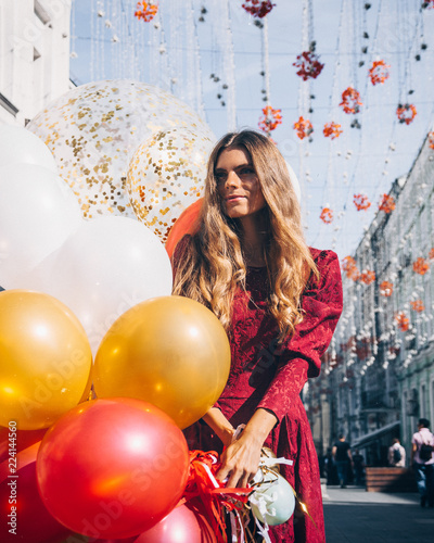 Beautiful woman in Red dress is so happy to walk with a lot of balloons