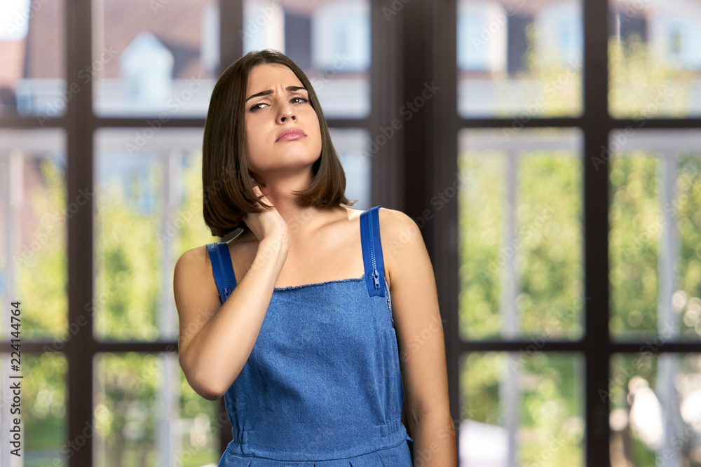 Young woman having neck pain. Pretty unhappy girl touching her nape on abstract window background. Pinched nerve concept. Young woman having neck pain. Pretty unhappy girl touching her nape on abstract window background. Pinched nerve concept.