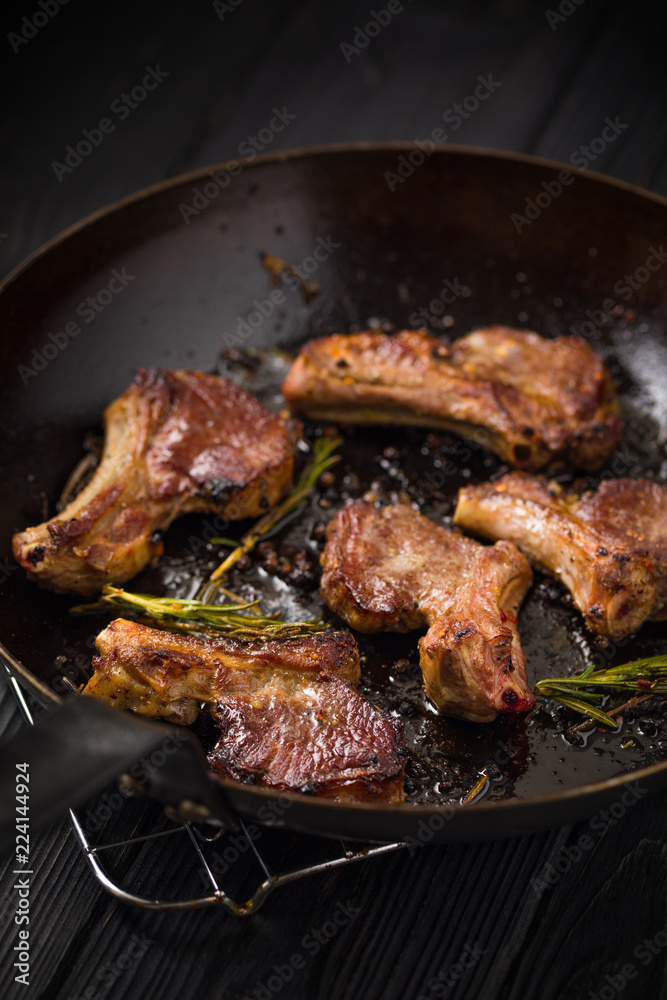 Lamb chops frying in a rustic metal pan with rosemary and mixed pepper