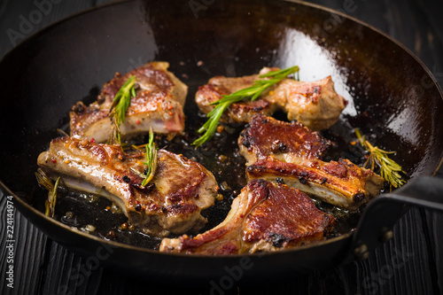 Lamb chops frying in a rustic metal pan with rosemary and mixed pepper