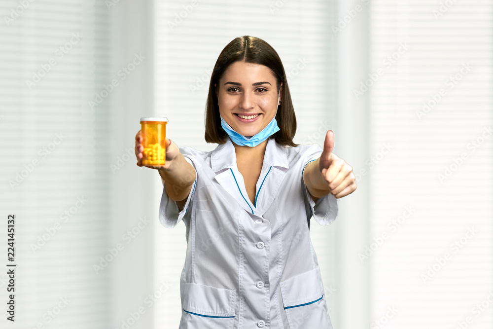Doctor with pills giving thumb up. Pretty female doctor showing pills and giving approval sign with finger. Doctor with pills giving thumb up. Pretty female doctor showing pills and giving approval sign with finger.