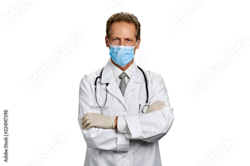 Portrait of medical doctor with arms crossed. Confident mature doctor in white coat and face mask folded his arms over white background.