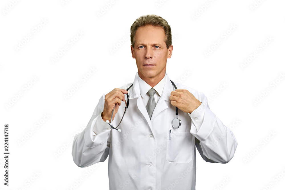 Doctor adjusting his stethoscope on white background. Male professional doctor in white coat looking seriously. Portrait of middle aged physician. Doctor adjusting his stethoscope on white background. Male professional doctor in white coat looking seriously. Portrait of middle aged physician.