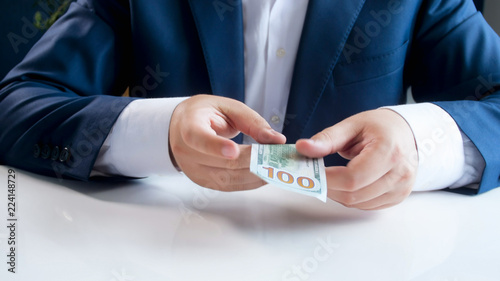 Closeup image of businessman sitting behind desk and holding 100 US dollars bill