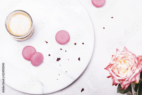 Morning glass of coffee and pink french cookies macaroons and rose flower on grey marble table and grey concrete background. Top view