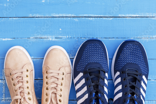 two pairs of male and female sports shoes on a blue wooden background