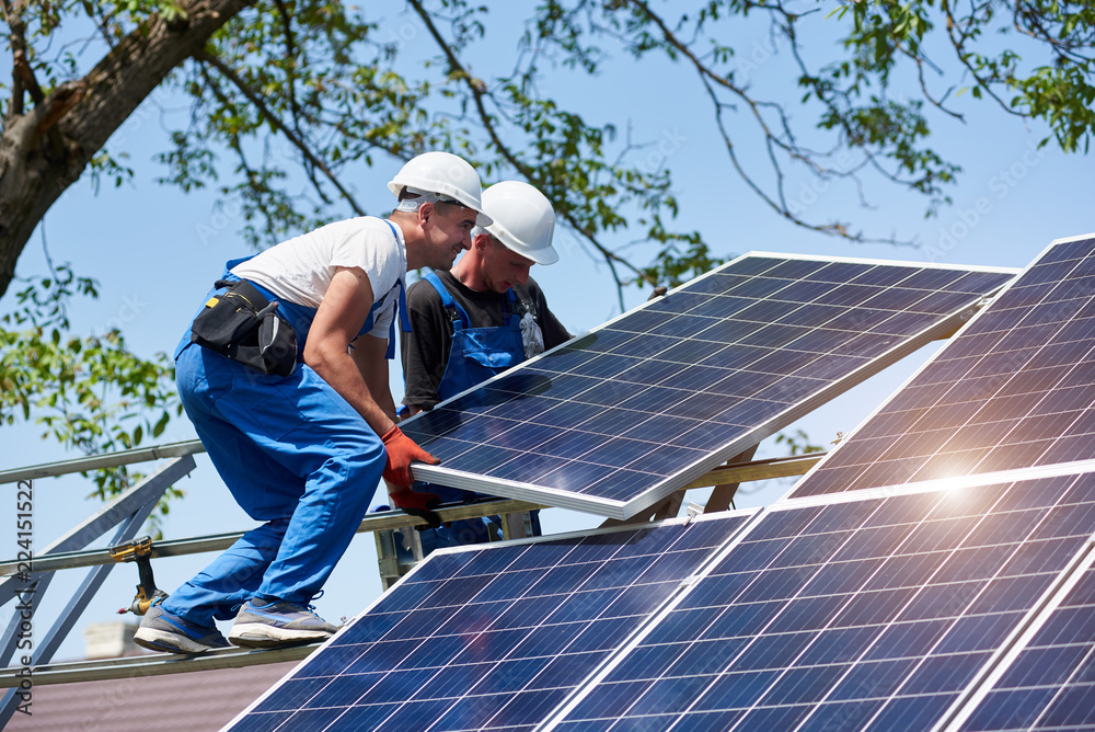 Ταπετσαρία Two young technicians installing heavy solar photo voltaic panel on tall steel platform on green tree background