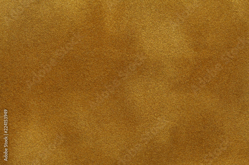 Background of dark golden suede fabric closeup. Velvet matt texture of yellow nubuck textile photo