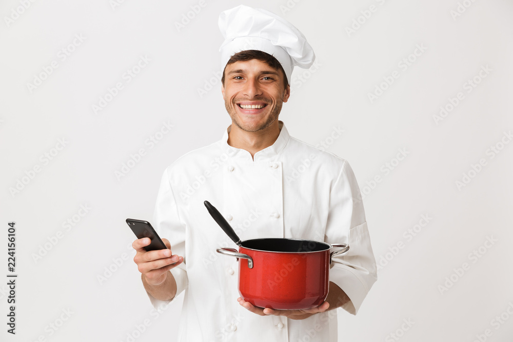 Young chef man standing isolated over white wall background holding crockery. Young chef man standing isolated over white wall background holding crockery.