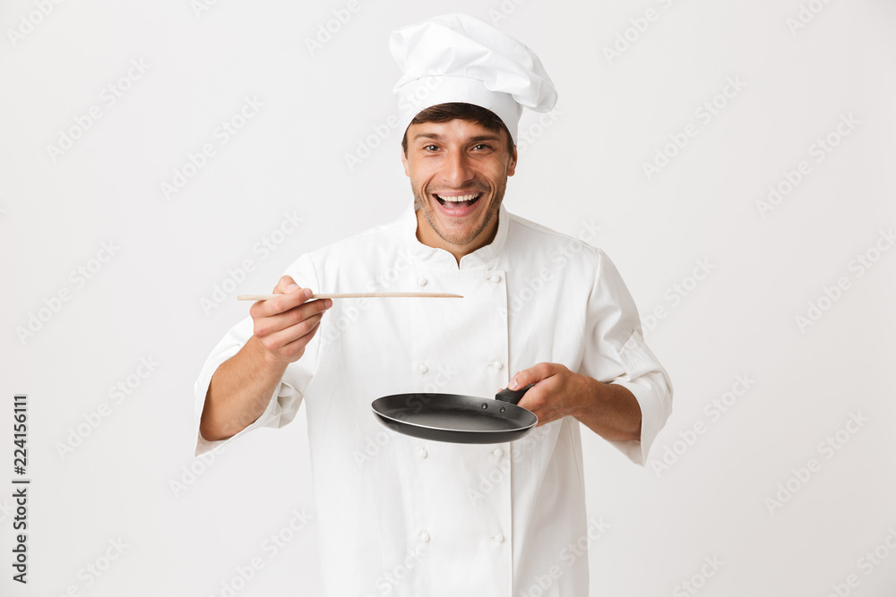 Young chef man standing isolated over white wall background holding crockery. Young chef man standing isolated over white wall background holding crockery.