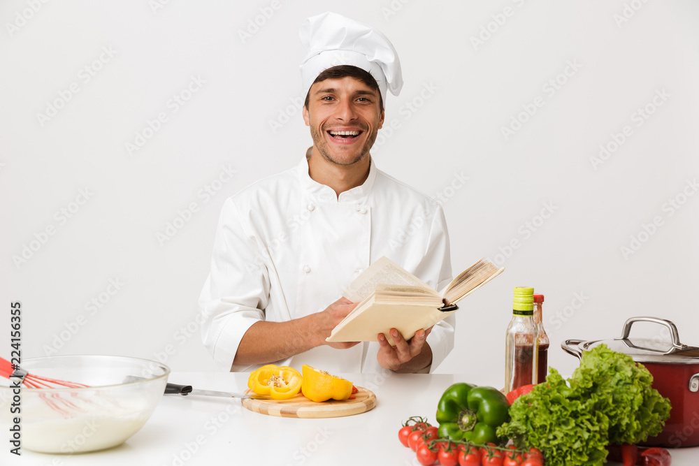 Young chef man isolated over white wall background cooking reading book. Young chef man isolated over white wall background cooking reading book.
