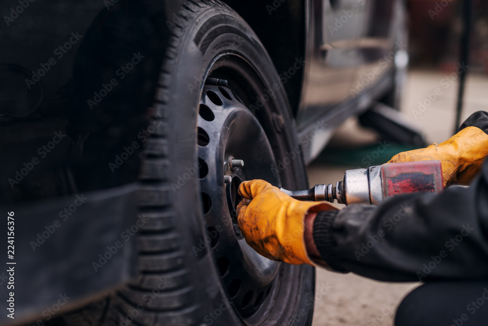 Fototapeta premium Auto mechanic with electric screwdriver changing tire outside. Car service. Tire installation.