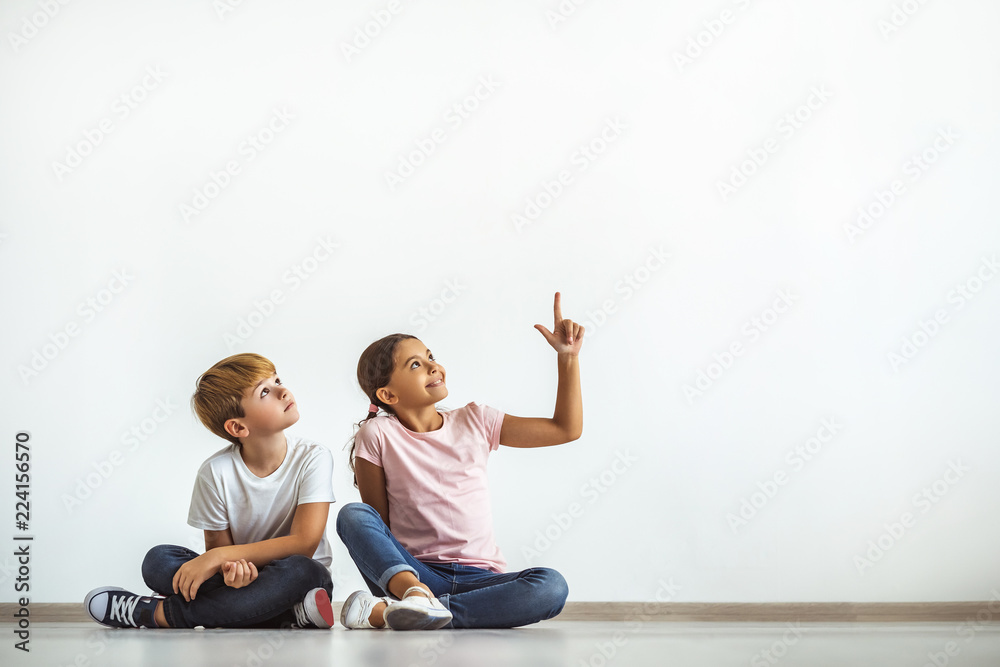 The happy girl and a boy sitting on the floor and gesturing - obrazy, fototapety, plakaty 