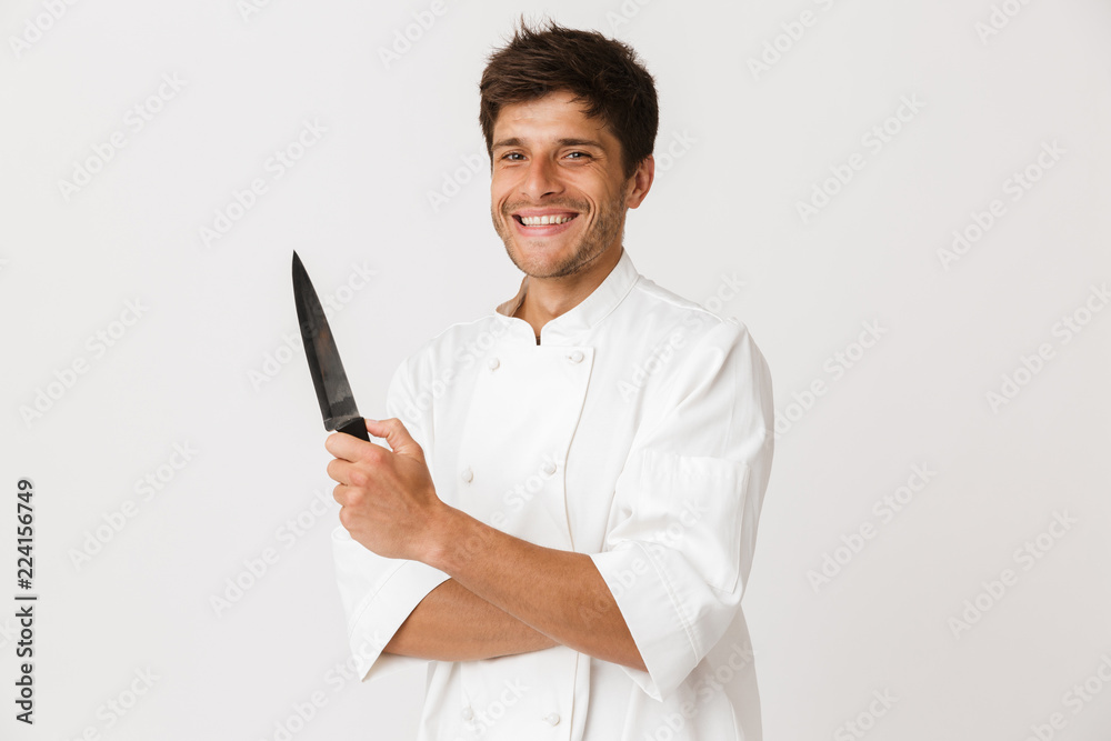 Young chef man standing isolated over white wall background holding knife. Young chef man standing isolated over white wall background holding knife.