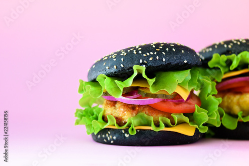 Macro view of tasty black burger with beef, cheese, lettuce, onion, tomatoes on yellow background. Close up banner. Unhealthy diet concept and copy space