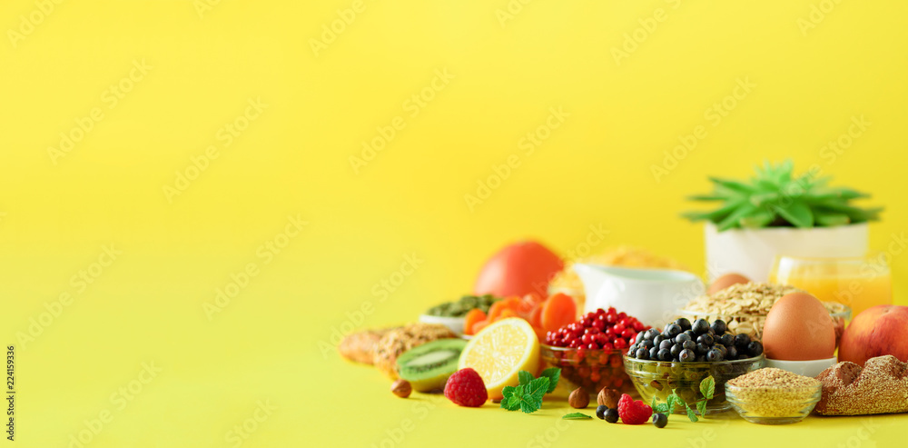 Vegetarian breakfast. Soft boiled egg, oat flakes, nuts, fruits, berries, milk, yogurt, orange, banana, peach on yellow background. Healthy food diet. Copy space. Banner