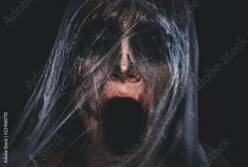 Photo Screaming creepy character covered with spiderweb on black background