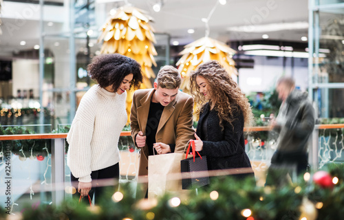 Young friends standing in shopping center at Christmas time, looking inside bags. photo