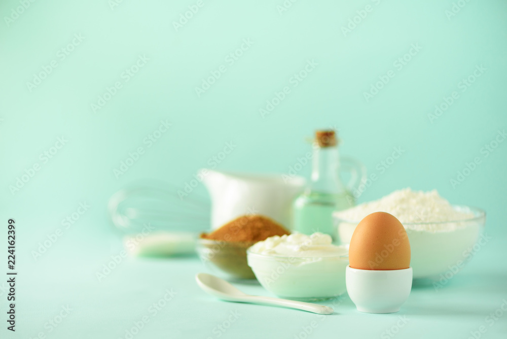 Time to bake. Baking ingredients - butter, sugar, flour, eggs, oil, spoon, brush, whisk, milk over blue background. Bakery food frame, cooking concept. Copy space