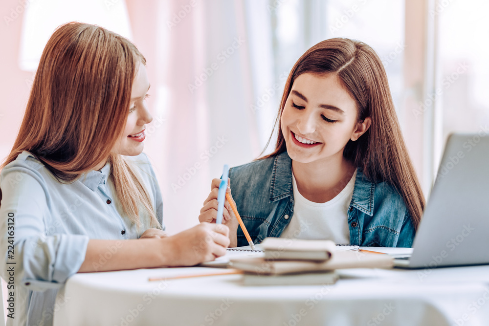 Keep smiling. Delighted brunette keeping smile on her face while helping her friend with lessons Keep smiling. Delighted brunette keeping smile on her face while helping her friend with lessons
