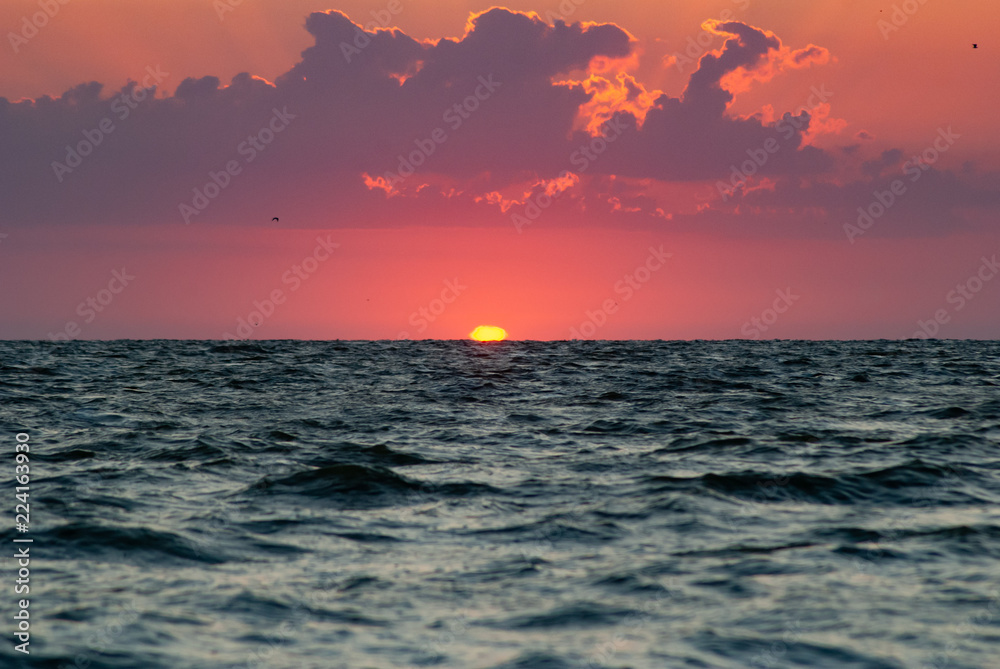 Dawn on the water, the sun over the horizon, a bright glow in the sky,