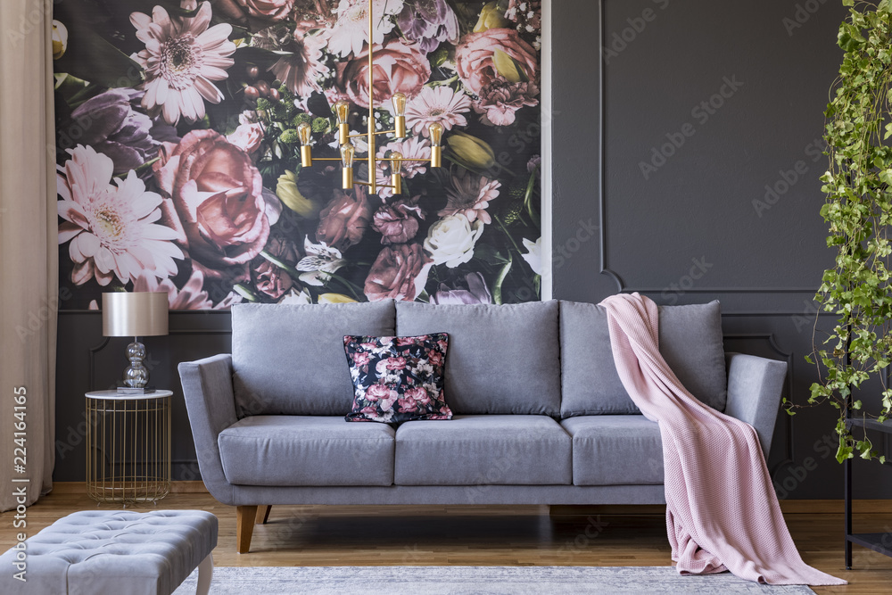 Real photo of a living room interior with a sofa, pillow, blanket and flowers on wallpaper - obrazy, fototapety, plakaty 