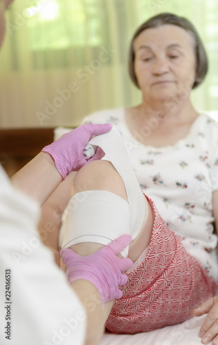 Doctor bandaging senior woman leg at home