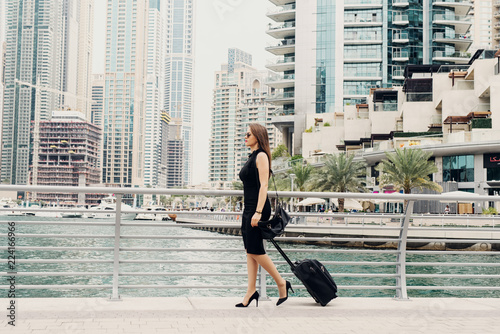 Young modern confident business woman pulling a suitcase in a Dubai Marine. Starting a new job in a big city. © dusanpetkovic1