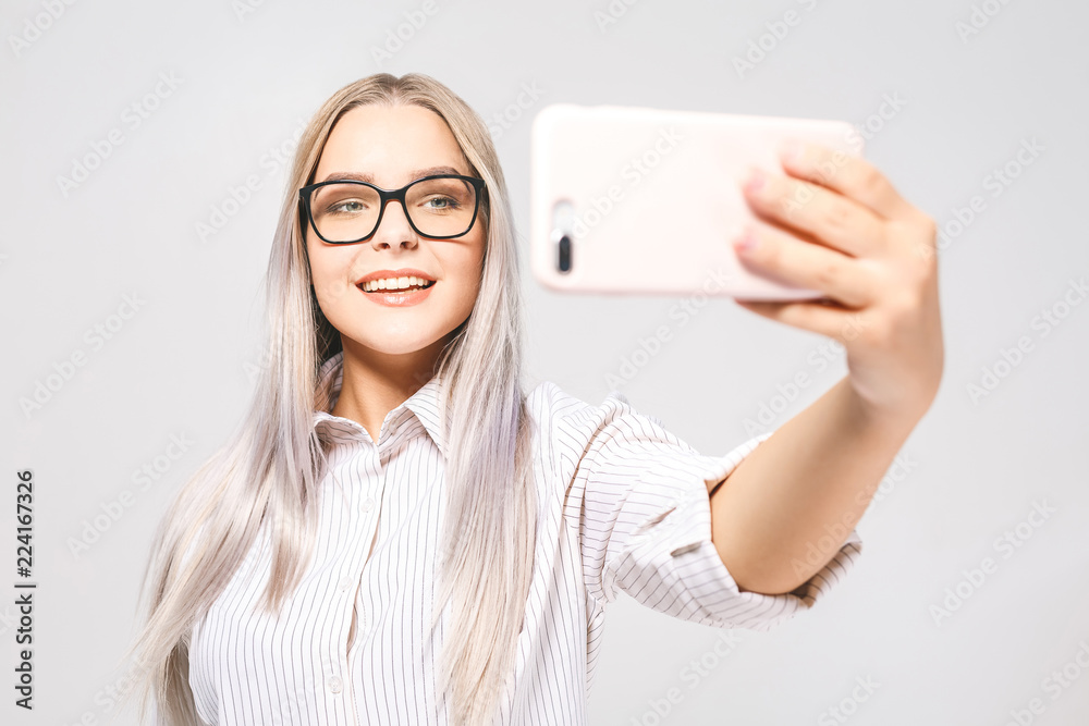 Portrait of a smiling cute woman in glasses making selfie photo on smartphone isolated on a white background. Portrait of a smiling cute woman in glasses making selfie photo on smartphone isolated on a white background.