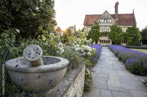 View of historic manor house from across a walled garden with lawn, path and flowerbeds.
