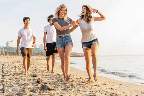 Group of friends having fun running down the beach at sunset.