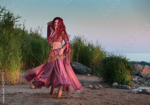 Beautiful young woman in Oriental dance costume by the sea.