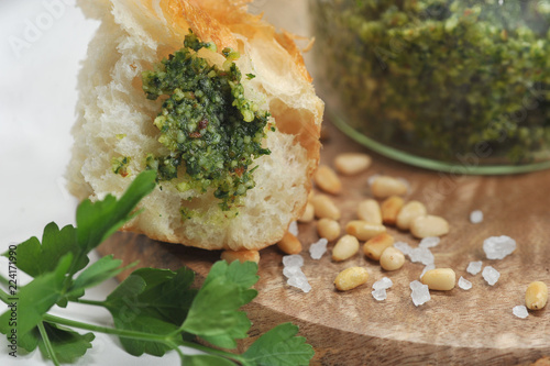 Green pesto sauce in a jar, large salt, pine nuts on a wooden plate. Pesto sauce is smeared onto a slice of ciabatta. Close-up. Macro photography.