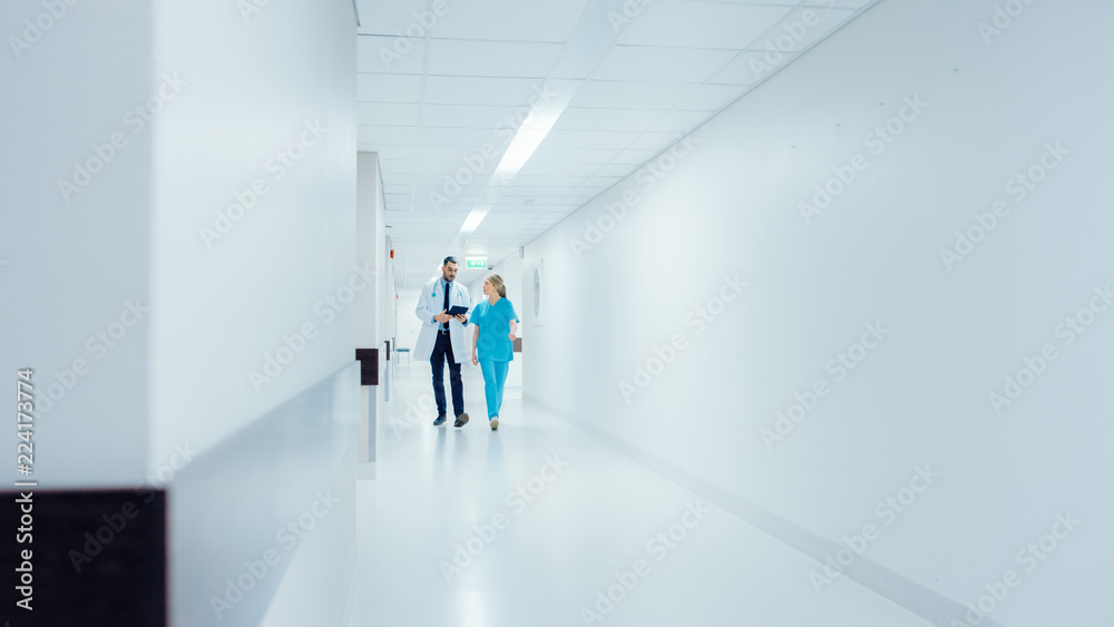 Surgeon and Female Doctor Walk Through Hospital Hallway in a Hurry while Using Digital Tablet and Talking about Patient's Health. Modern Bright Hospital with Professional Staff. Surgeon and Female Doctor Walk Through Hospital Hallway in a Hurry while Using Digital Tablet and Talking about Patient's Health. Modern Bright Hospital with Professional Staff.