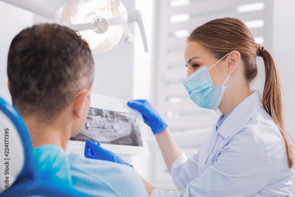 Good results. Young skilled dental roentgenologist holding the results of an X ray and showing them to her attentive patient Good results. Young skilled dental roentgenologist holding the results of an X ray and showing them to her attentive patient