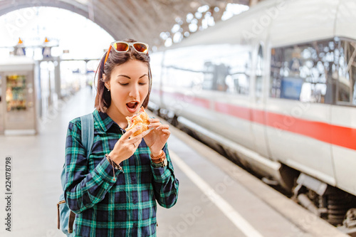 Healthy young woman biting her hamburger at railway station near fast train