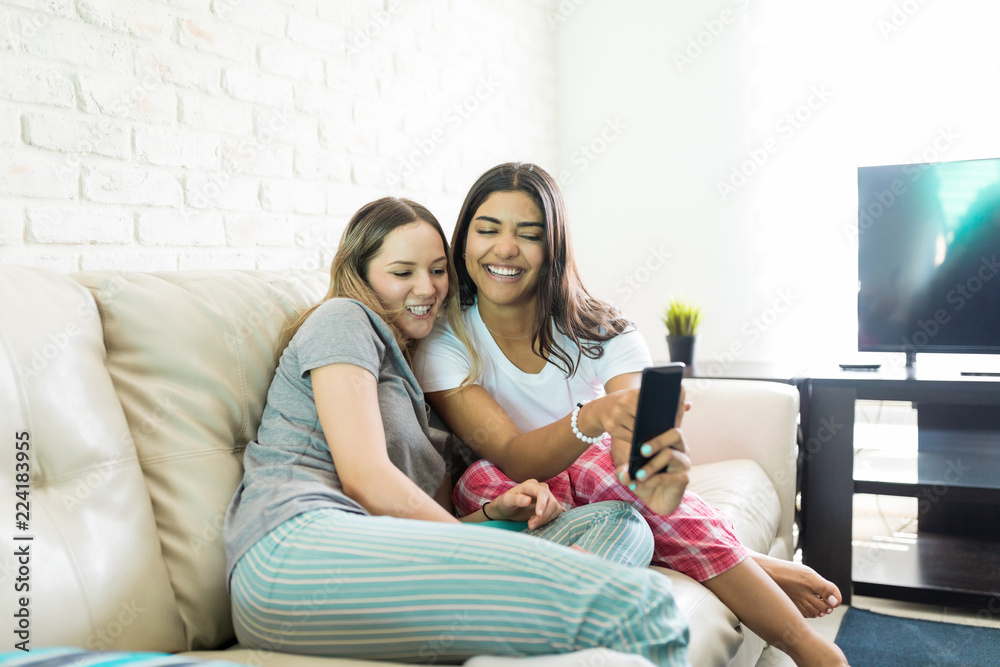 Friends Looking At Funny Pictures On Smartphone During Sleepover Party Friends Looking At Funny Pictures On Smartphone During Sleepover Party