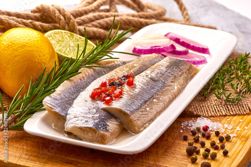 Obraz na płótnie Atlantic Marinated herring fillet with pepper, tomatoes, herbs, onion and lemon on white plate on cutting board