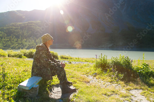 A man sitting on a bench meets the dawn. A tourist is sitting at dawn near a mountain lake.