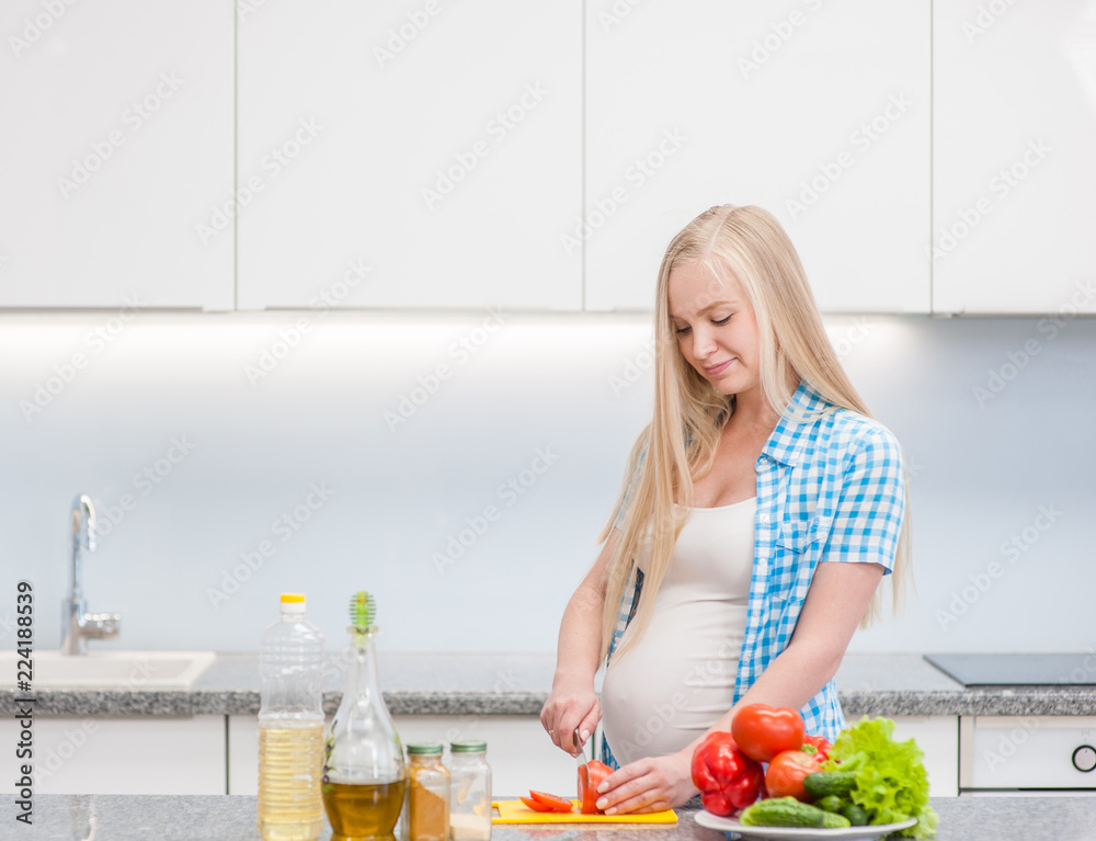 Happy pregnant woman at kitchen prepares a vegetable salad. Space for text