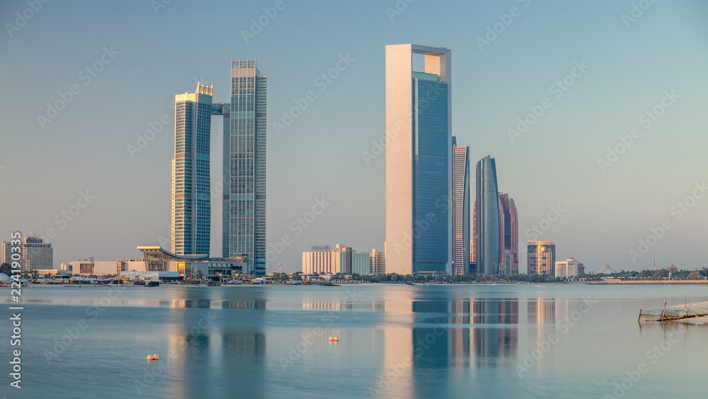 Fototapeta premium Abu Dhabi city skyline with skyscrapers after sunrise with water reflection timelapse